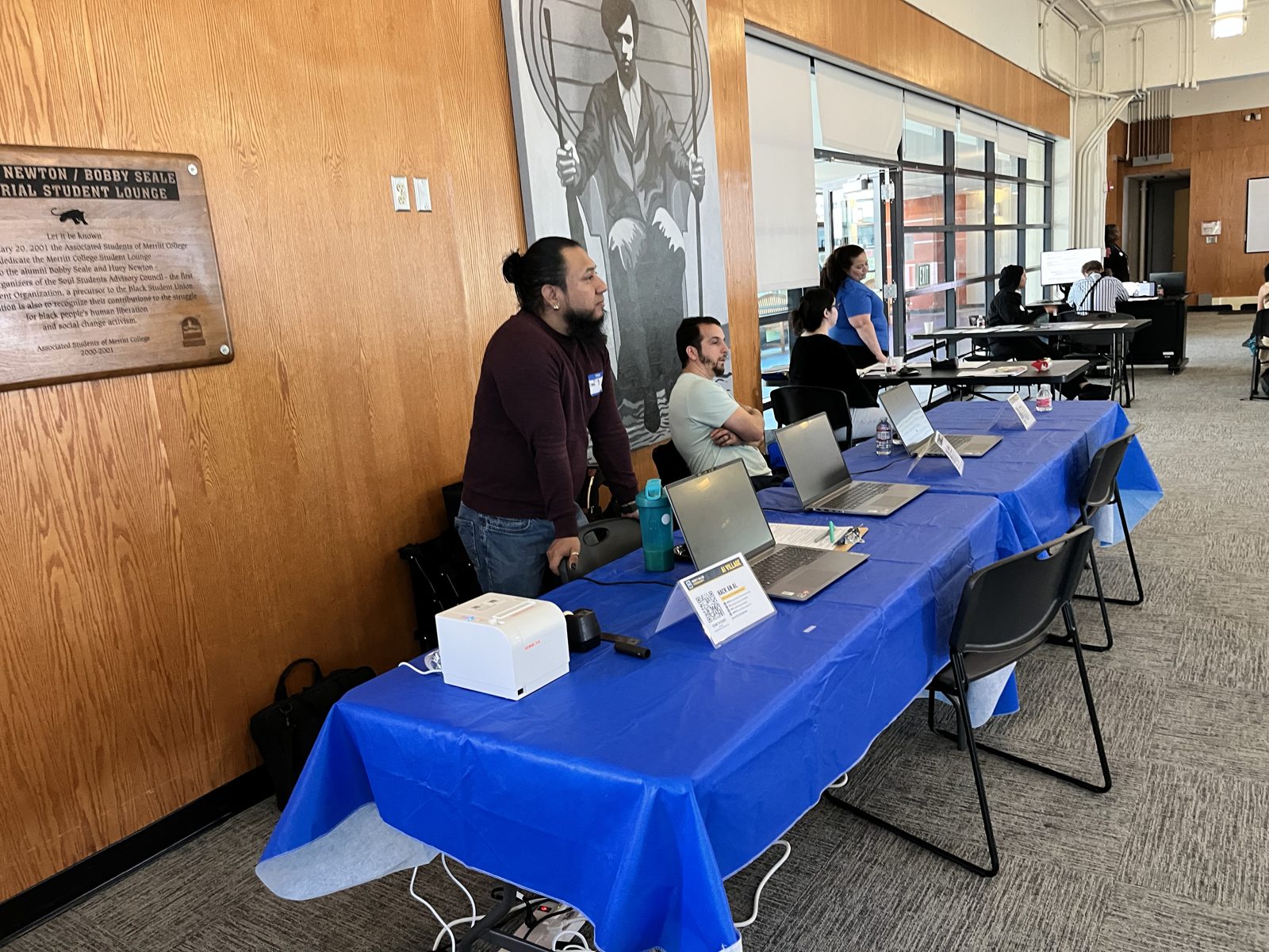The AI Village booth: receipt printer, table tent and three laptops on a blue table
